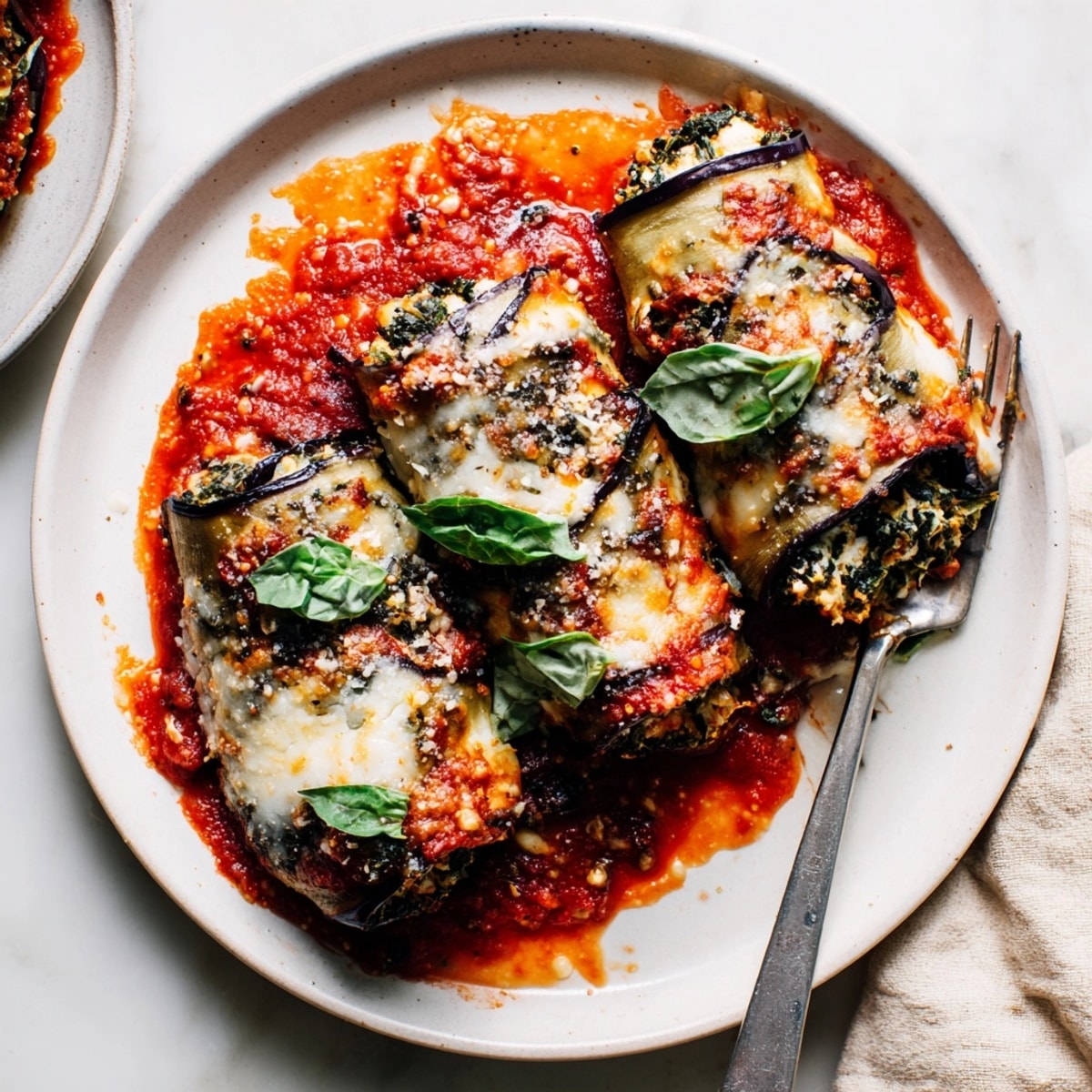 Golden baked Eggplant Rollatini filled with creamy ricotta and spinach on a saucy plate.