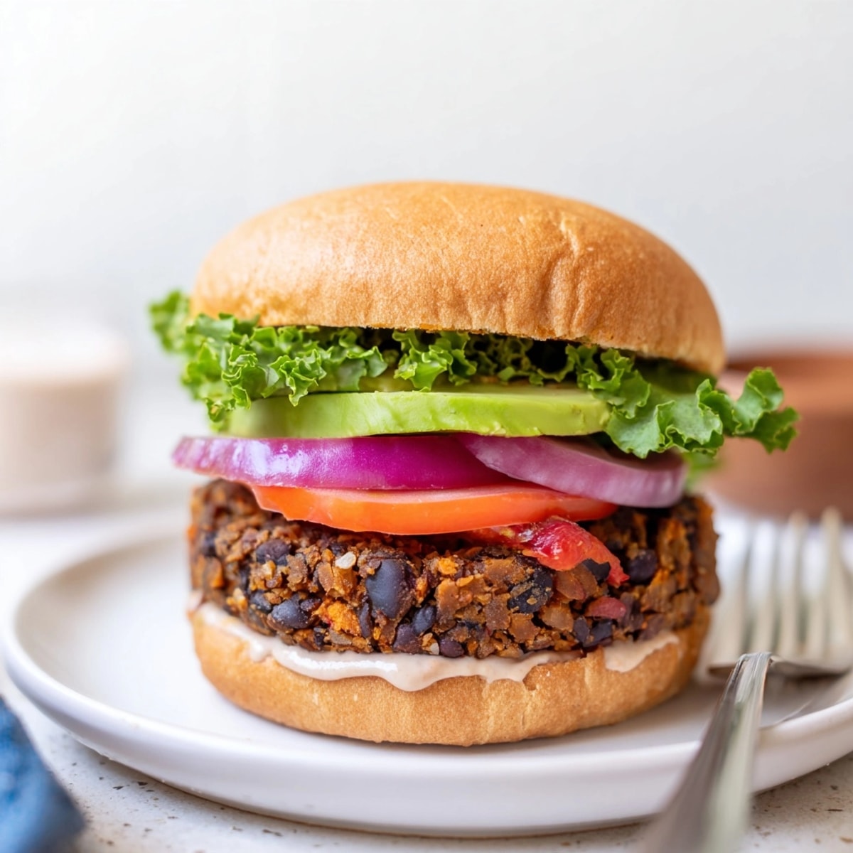 Close-up of a juicy Sweet Potato Black Bean Burger stacked high with toppings.