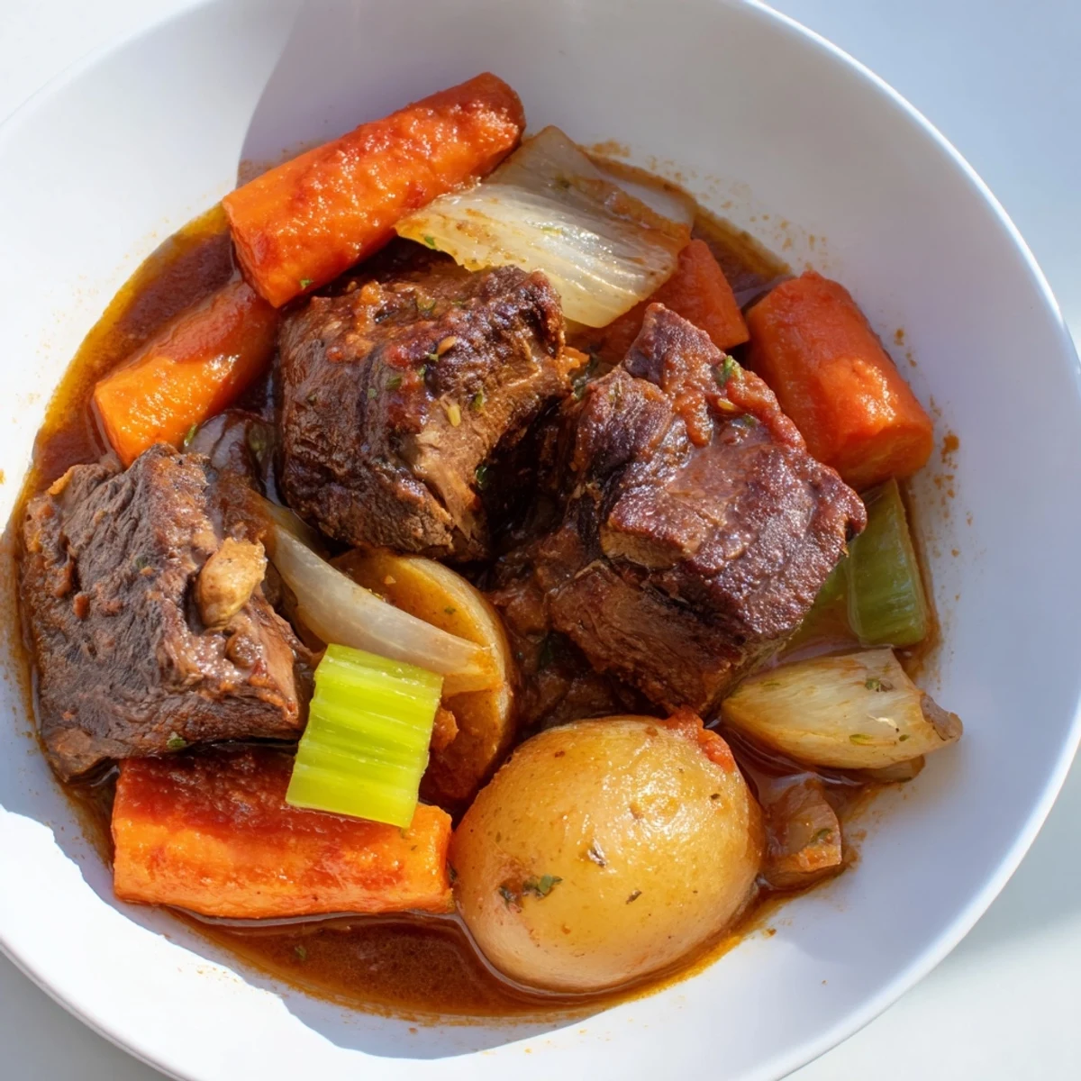 A steaming bowl of comforting bone-in beef stew, filled with chunks of beef and carrots.