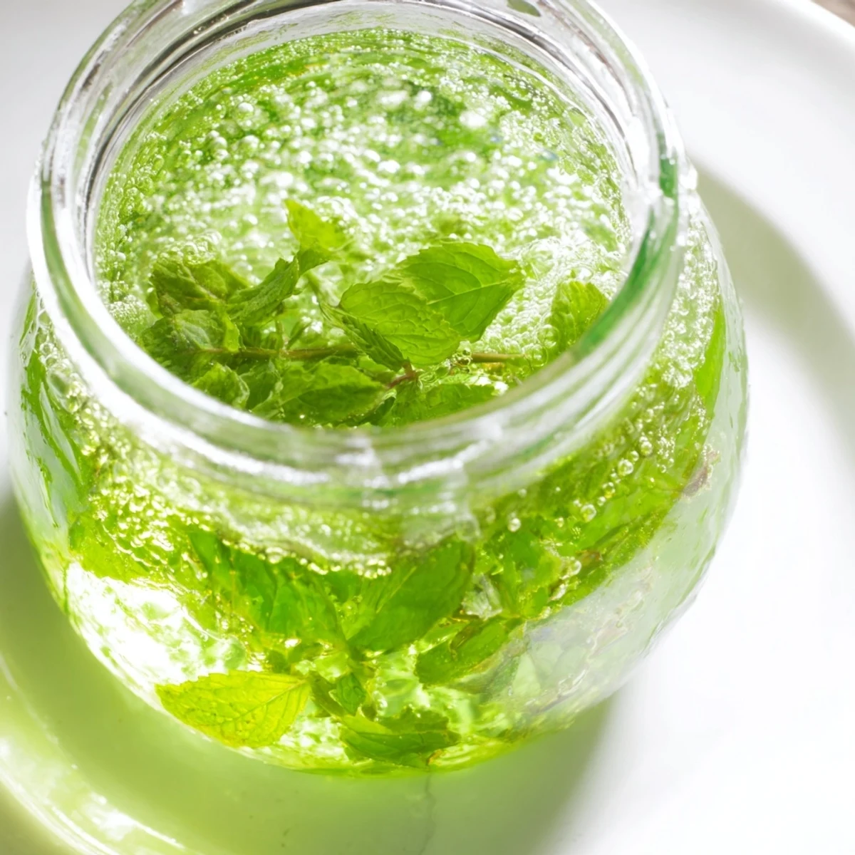 Clear glass bottle of fresh peppermint syrup, vividly showcasing its bright green hue.