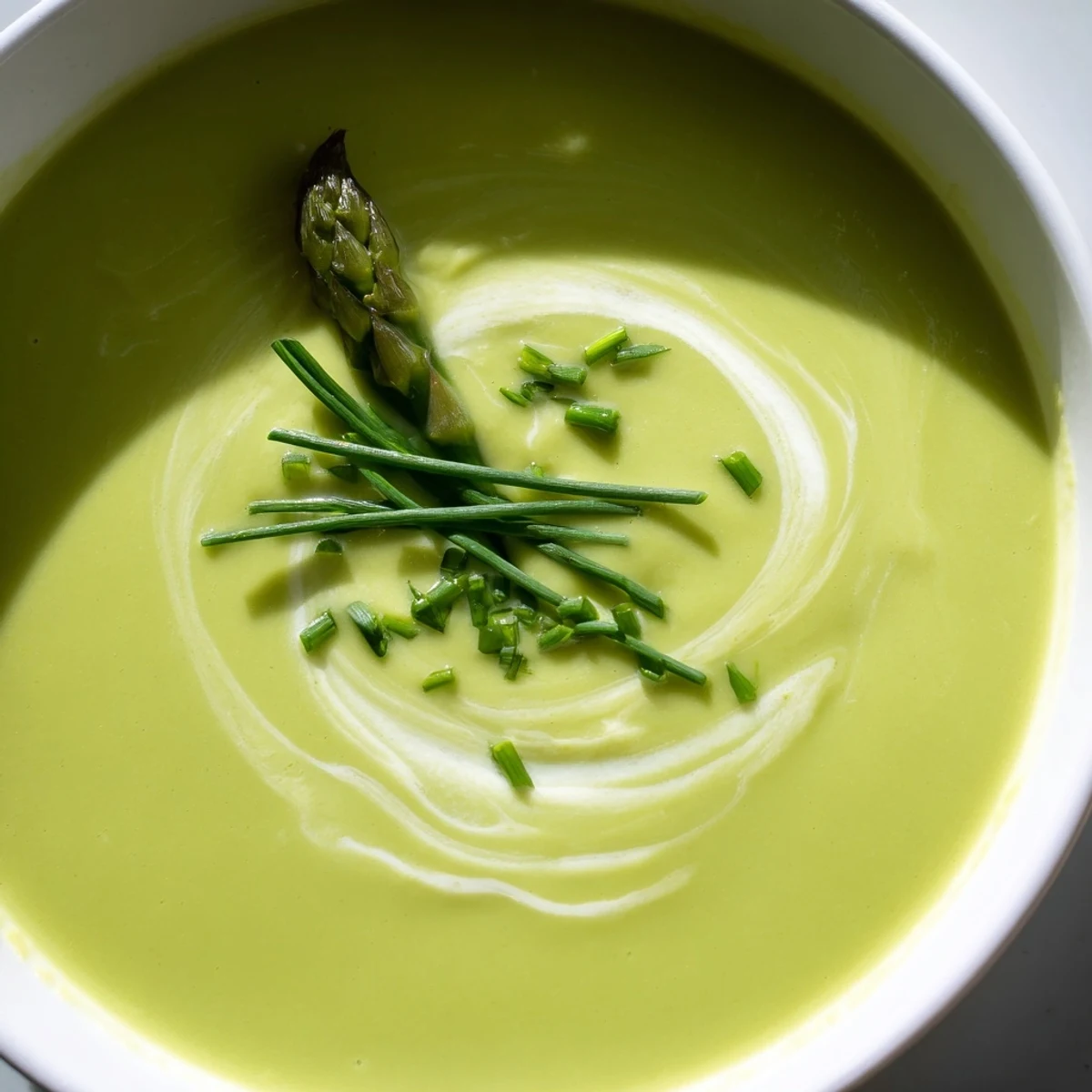 Bright green Creamy Asparagus Soup with Lemon and Crème Fraîche topped with fresh chives, ready to serve.