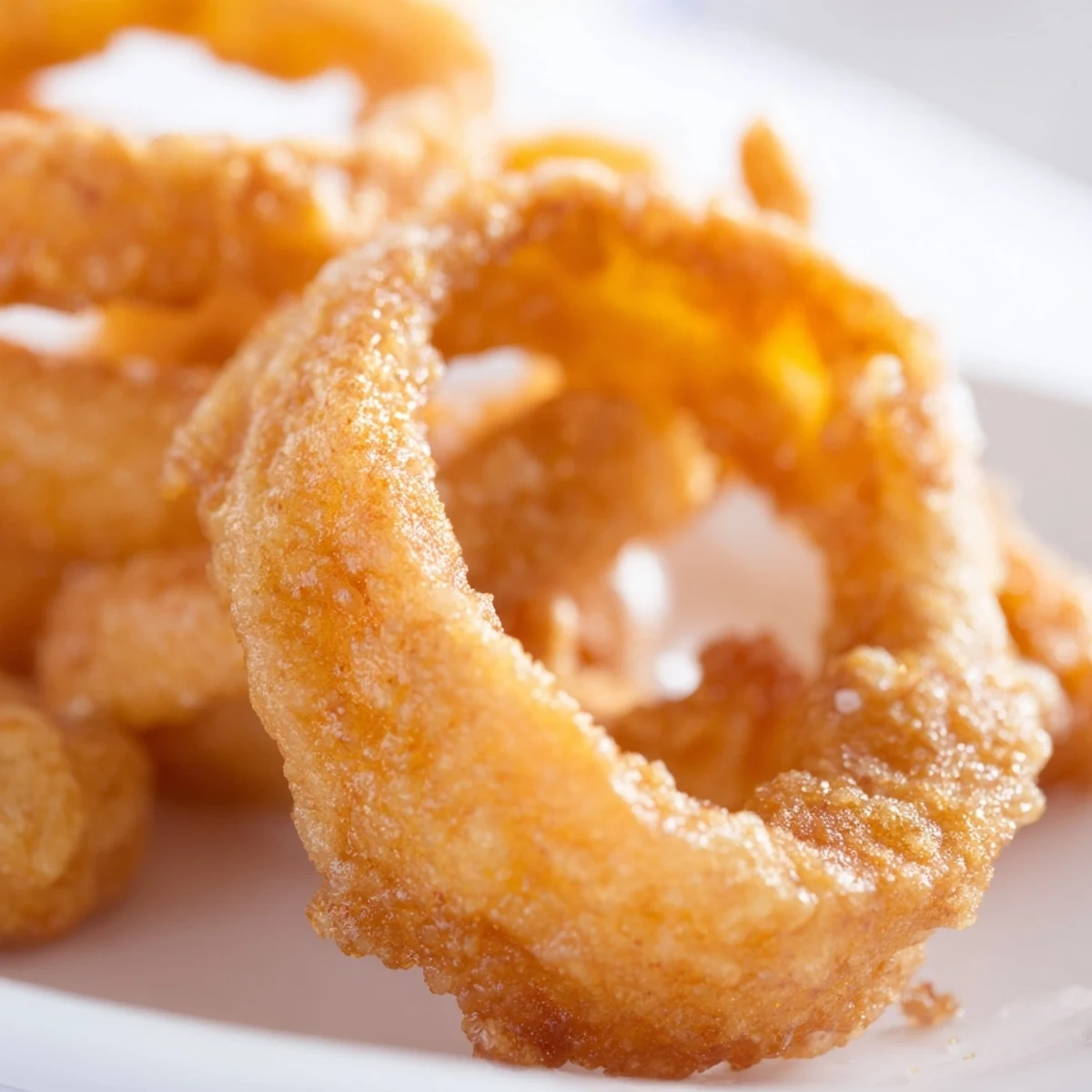 Golden brown Crispy Onion Rings with Batter rest on paper towels, sprinkled with sea salt and served with dipping sauces.