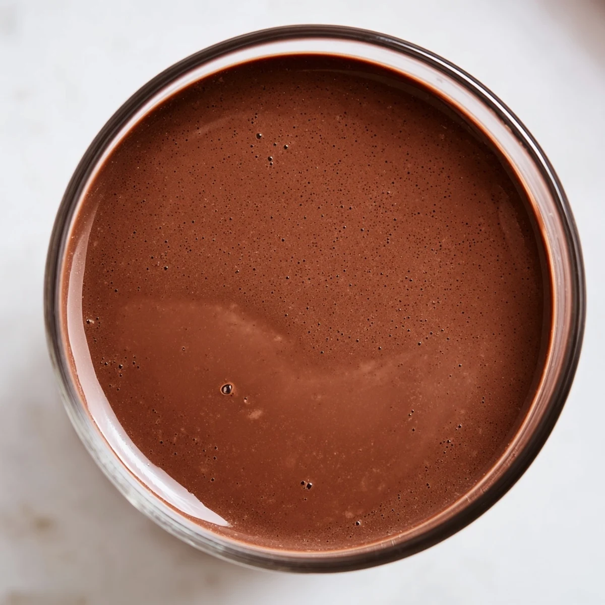 Creamy chocolate milk in a glass with ice, prepared with cocoa powder and sugar, ready to drink.
