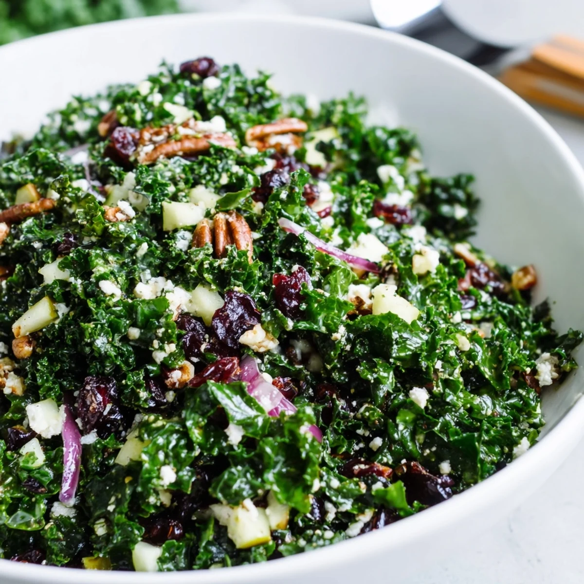 Winter Kale Salad with Cranberries plated beside a glass of sparkling water, showcasing diced apples, red onion slices, and crunchy nuts for a healthy lunch.