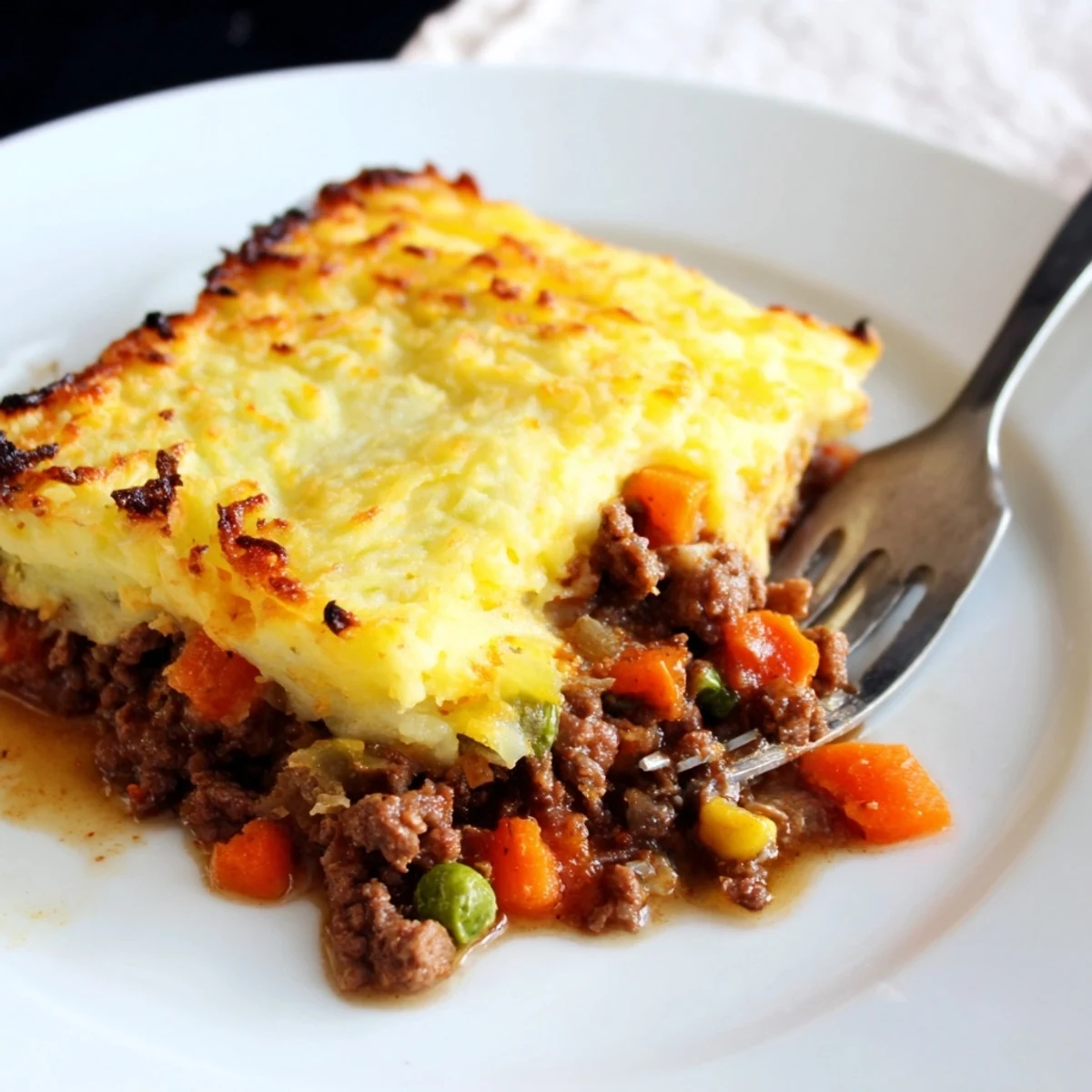 Savory beef filling peeking through crusty, cheesy mashed potato peaks in a baking dish.
