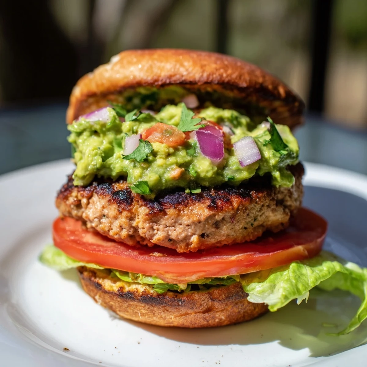 Golden-brown turkey burger patties resting in a skillet, topped with a generous scoop of chunky guacamole and fresh cilantro.