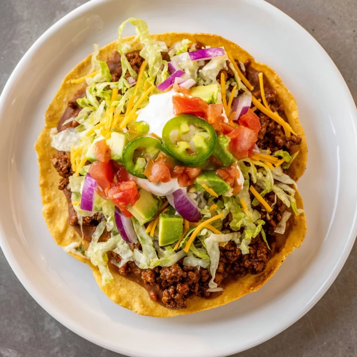 Colorful fresh toppings like shredded lettuce, diced tomatoes, and avocado add vibrant texture and flavor to the plated Beef Tostadas.