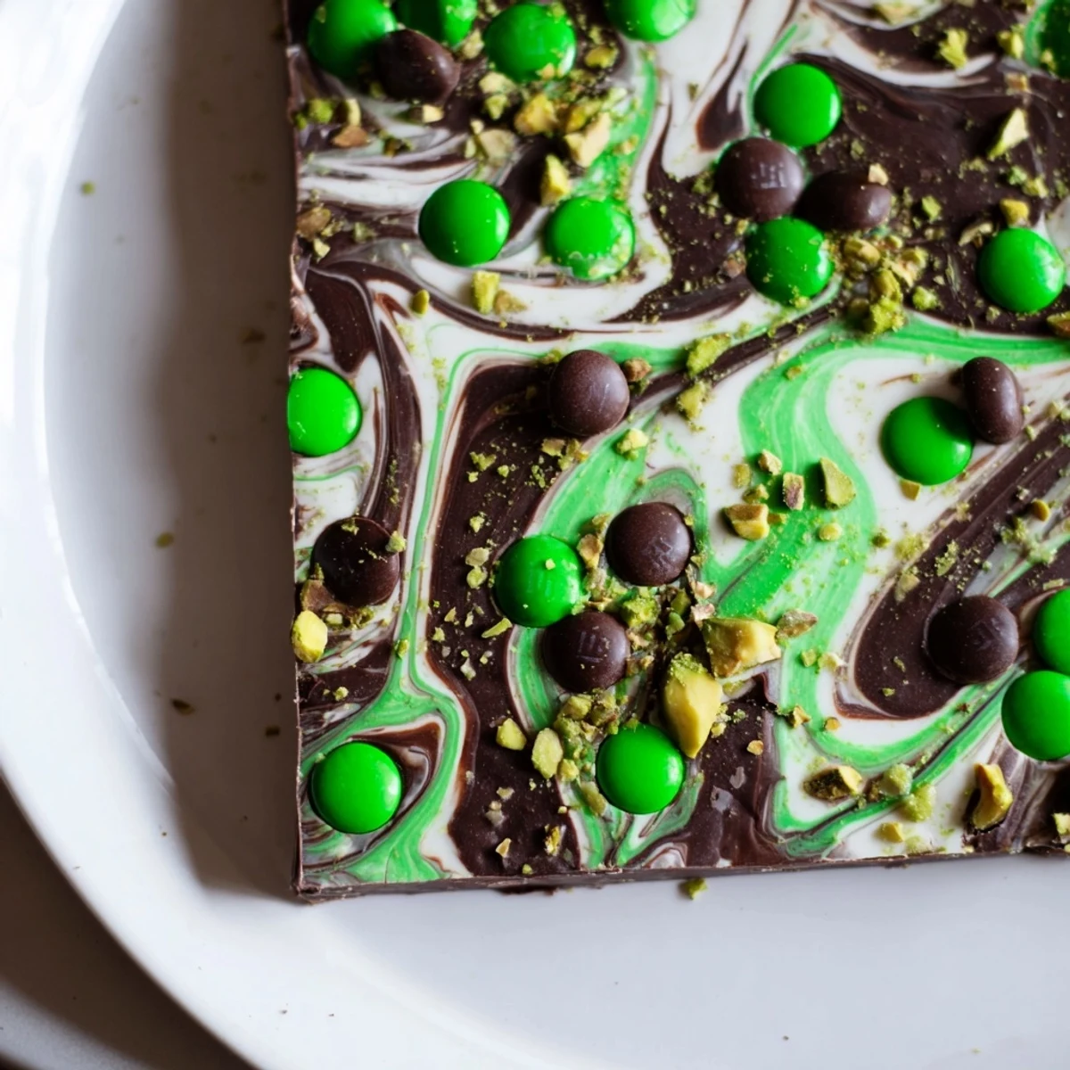 Break apart a piece of St. Patrick's Day Mint Chocolate Bark to reveal its smooth, mint-infused layers and crunchy green toppings, perfect for a holiday dessert spread.