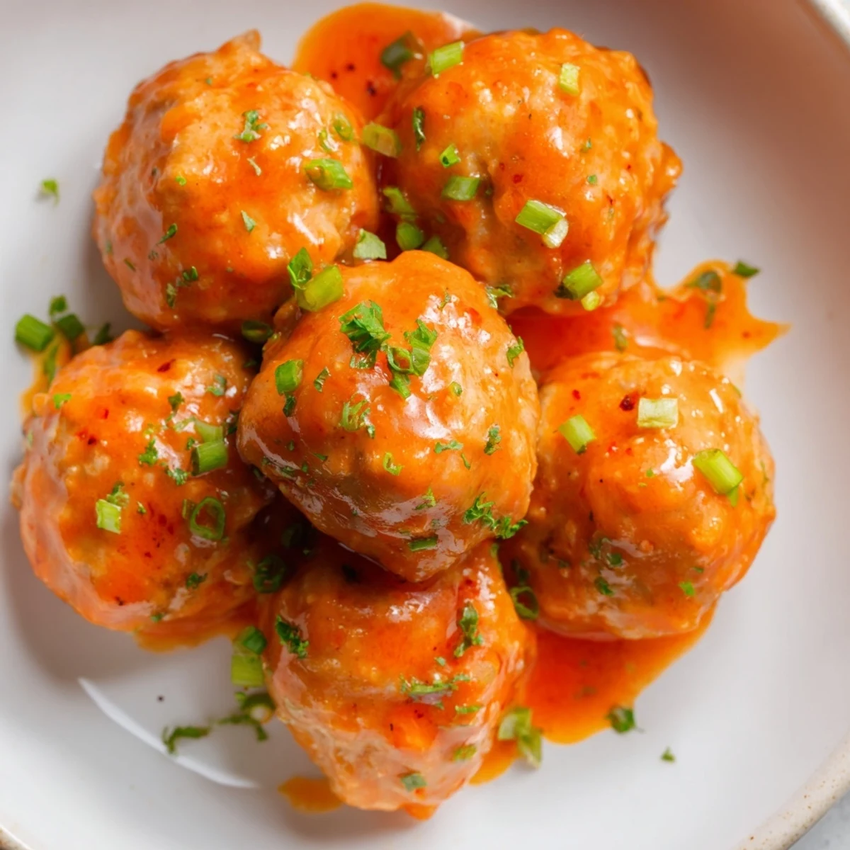 Golden brown Touchdown Buffalo Chicken Meatballs coated in a glossy, spicy red buffalo sauce garnished with fresh parsley.