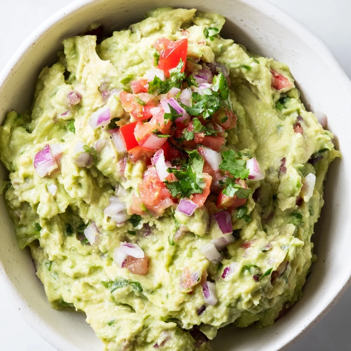 A close-up of Super Bowl Guacamole with Salsa, creamy and dotted with red onion, jalapeño, and fresh cilantro.