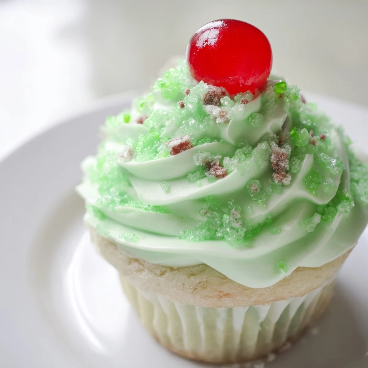 Close-up of a Shamrock Shake Cupcake with fluffy whipped mint frosting, green sprinkles, and a maraschino cherry on top.