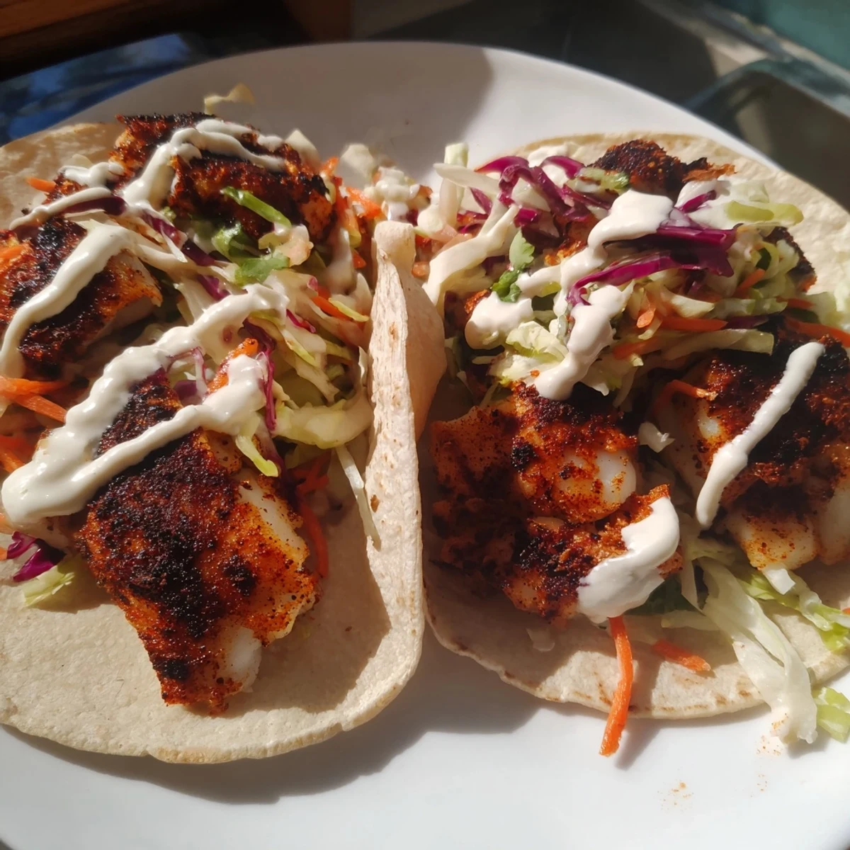 Golden-brown blackened fish tucked into warm corn tortillas, topped with crunchy purple cabbage slaw and a swirl of zesty crema.