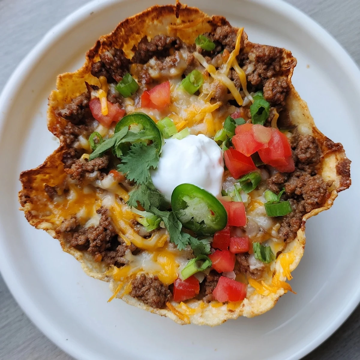 Crispy, golden Taco Cups with Ground Beef and Cheese baked in a muffin tin, topped with sour cream and fresh cilantro for a Tex-Mex appetizer.