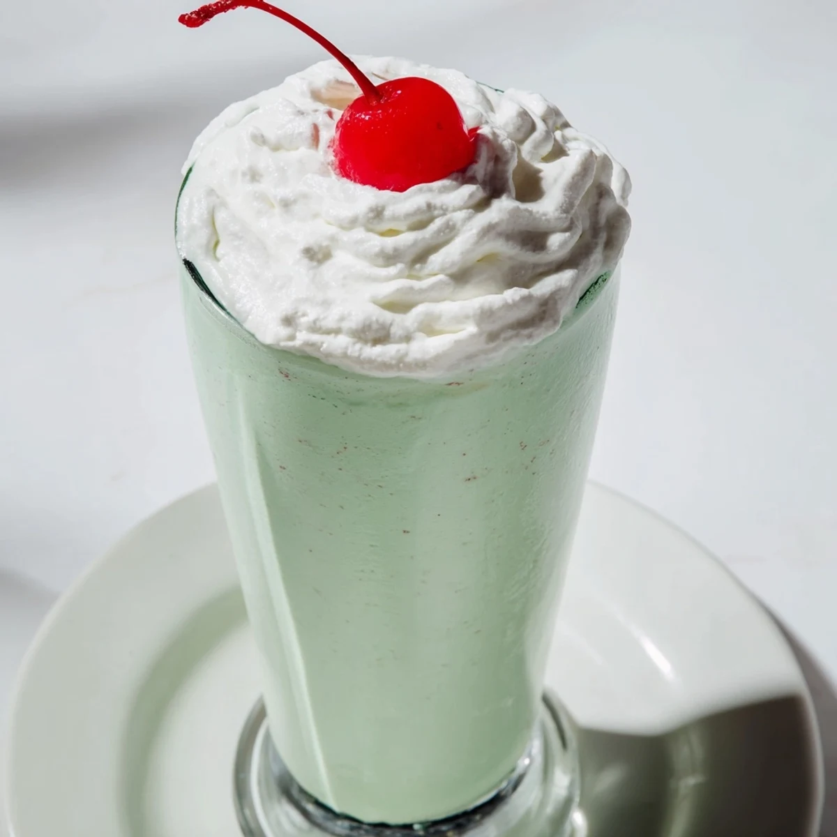 Refreshing mint milkshake with maraschino cherry, featuring creamy vanilla ice cream and a sweet, festive cherry on top.