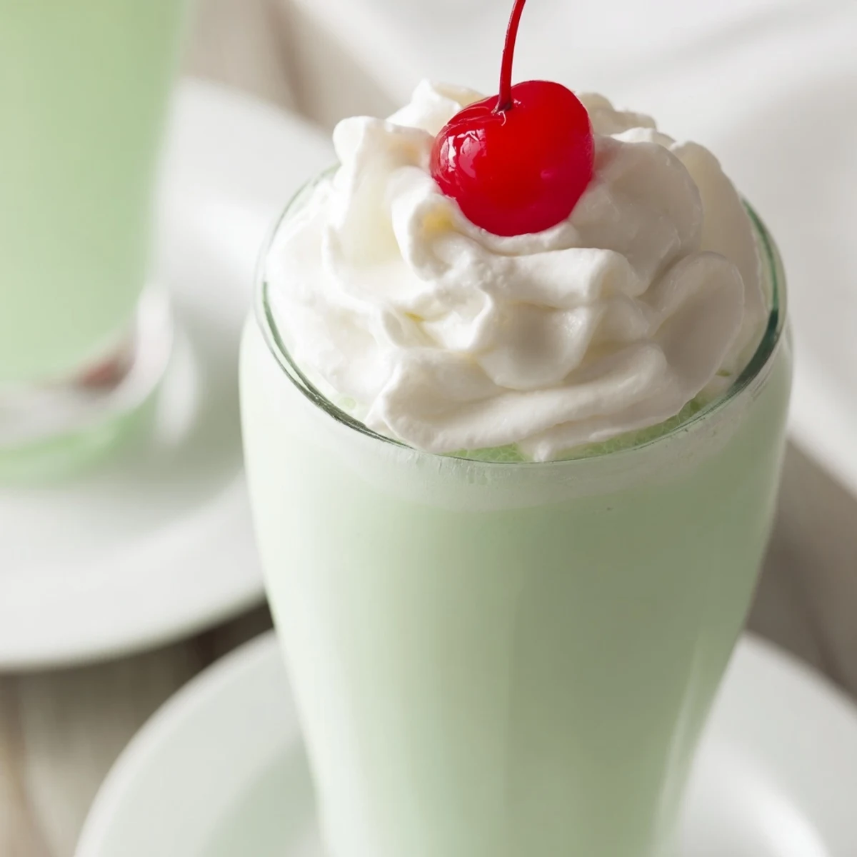 Two chilled glasses of homemade mint milkshake with maraschino cherry garnish, ready to sip on a hot day.