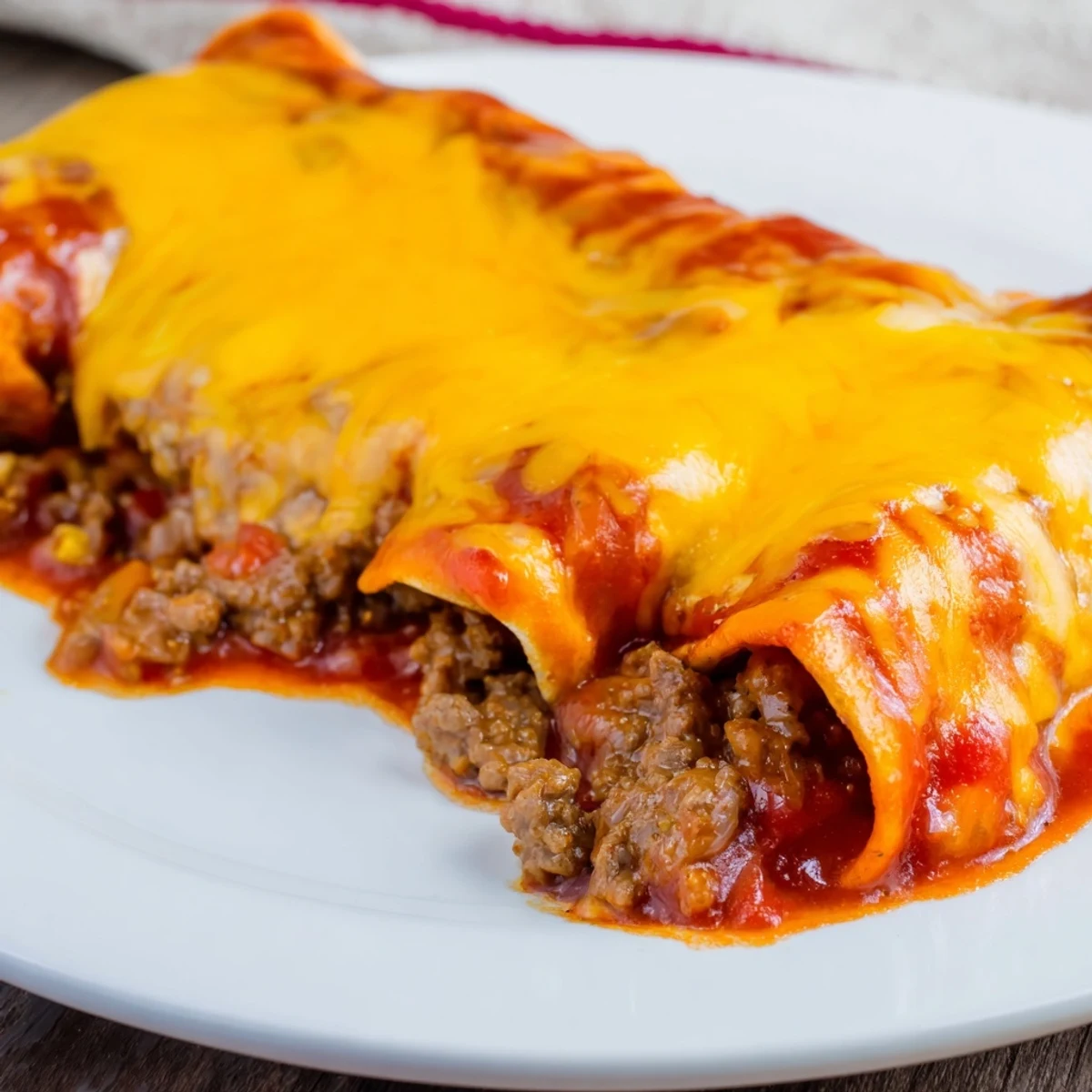 Serving suggestion for Beef Enchiladas with Red Enchilada Sauce, plated with sliced avocado and a dollop of sour cream beside a vibrant salad.