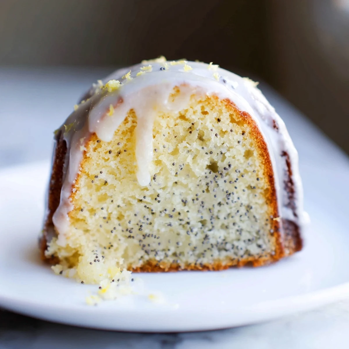 A slice of Lemon Poppy Seed Bundt Cake with Glaze shows moist crumb and glossy icing on a white plate.