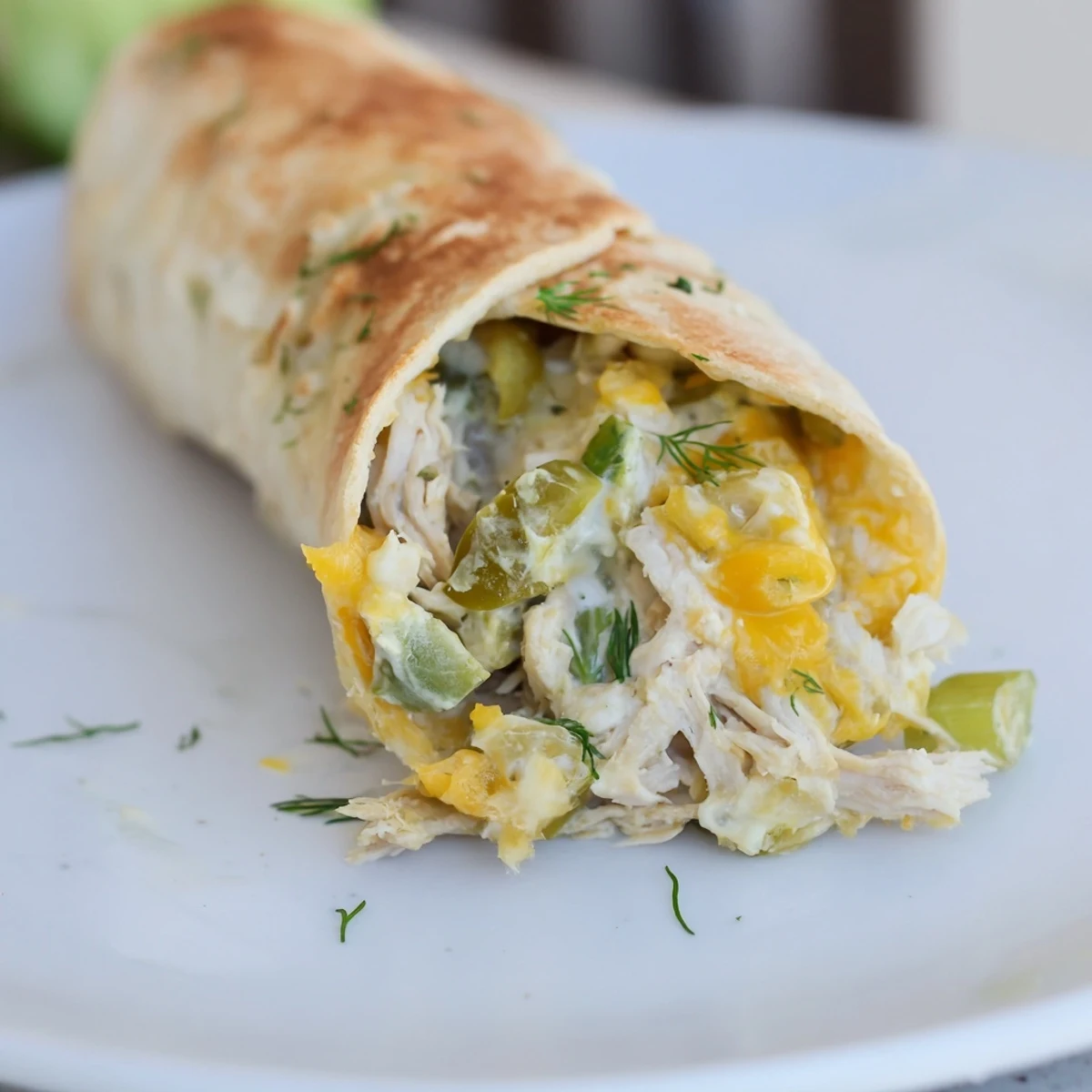Golden-baked Dill Pickle Ranch Chicken Taquitos rest on a rustic wooden board, showcasing their crispy, golden-brown tortilla shells that encase a savory filling of shredded chicken, green dill pickle specks, and melted cheddar. Fresh dill sprigs and a small bowl of creamy white ranch dipping sauce sit beside them on a checkered napkin.
