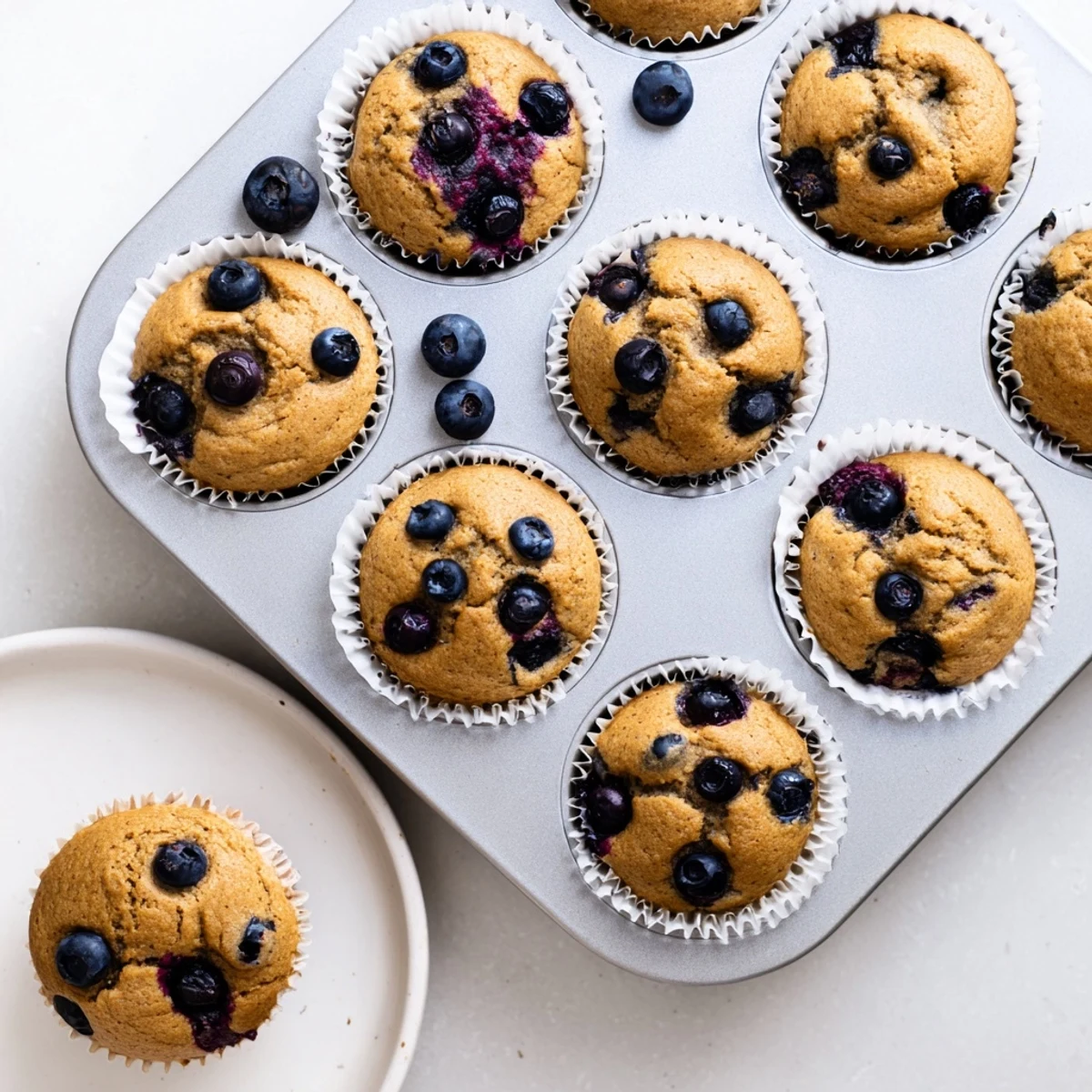 Freshly baked Greek Yogurt Blueberry Protein Muffins arranged on a white plate with a side of coffee.