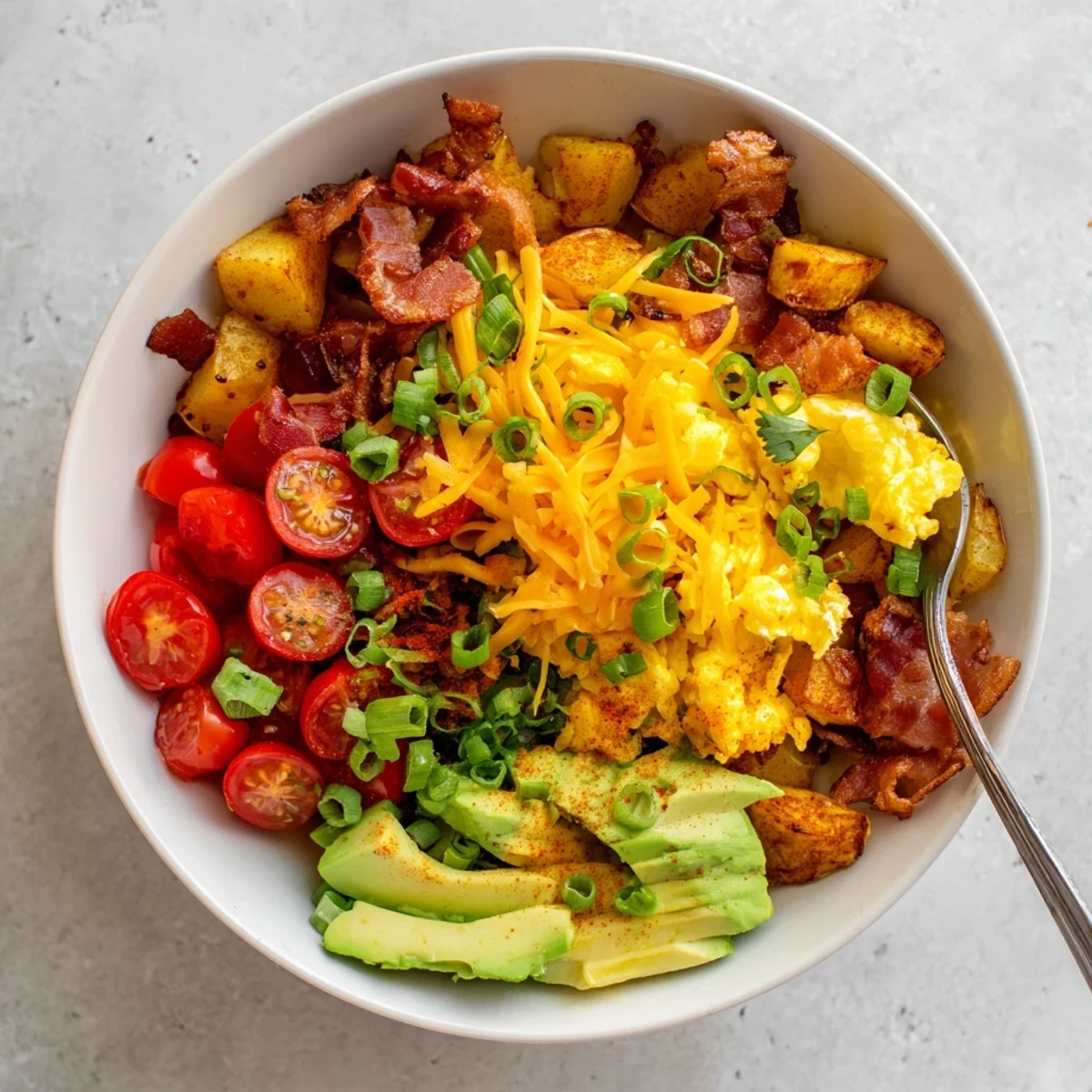 A warm Loaded Breakfast Bowl garnished with cherry tomatoes and cheddar cheese, ready to enjoy.