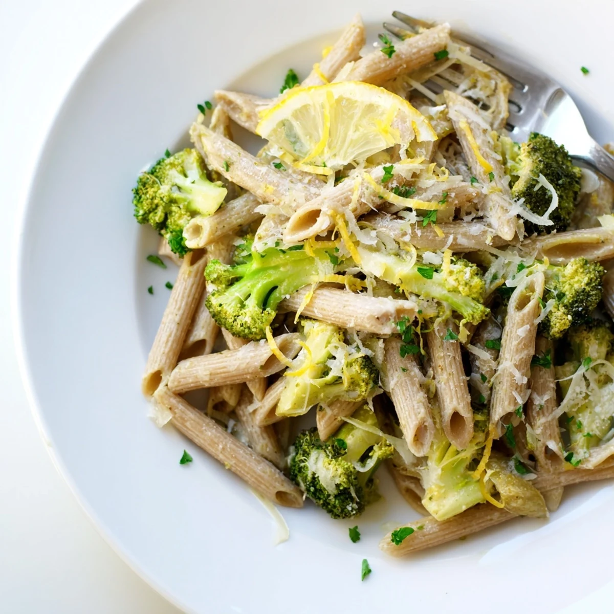 A close-up of Easy Healthy Broccoli Pasta with bright green florets on whole wheat penne in a glossy olive oil sauce, sprinkled with Parmesan and fresh parsley.