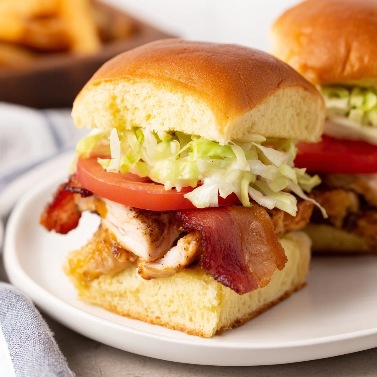 Golden toasted slider buns holding juicy baked chicken, crisp bacon, fresh lettuce, and ripe tomato with a honey mustard drizzle.