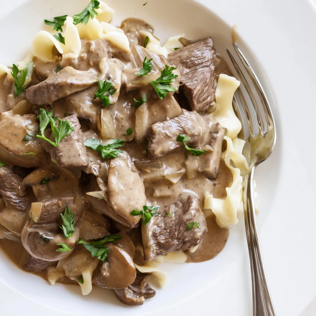 Homemade beef and mushroom stroganoff plated on egg noodles with chopped parsley topping
