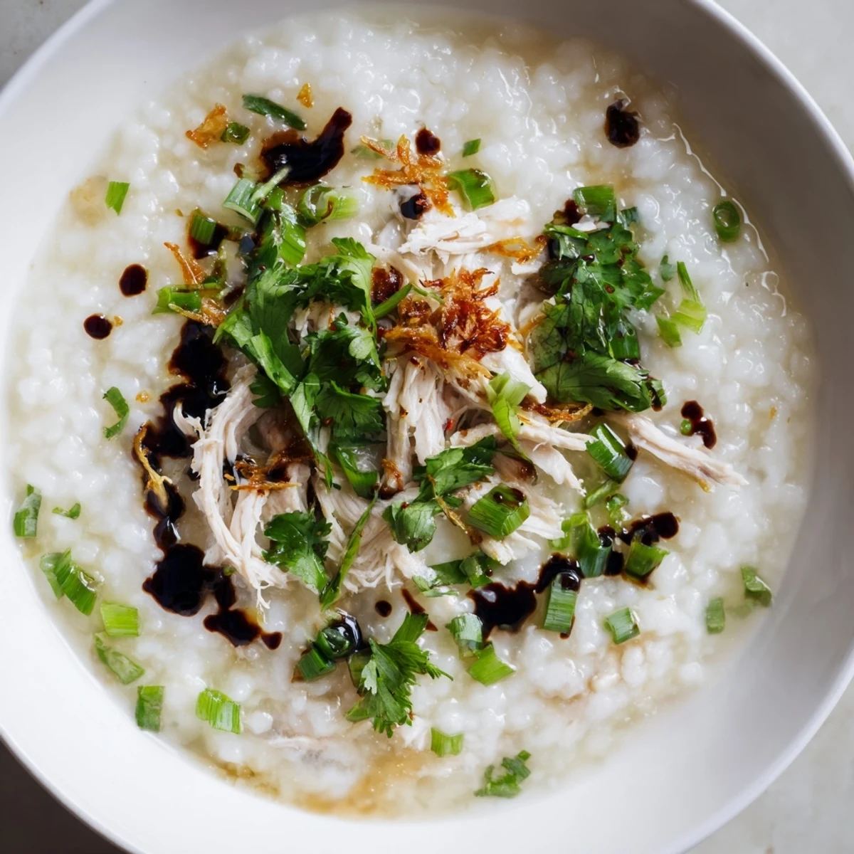 Creamy leftover Thanksgiving turkey congee topped with fresh scallions, cilantro, and crispy shallots in a white bowl