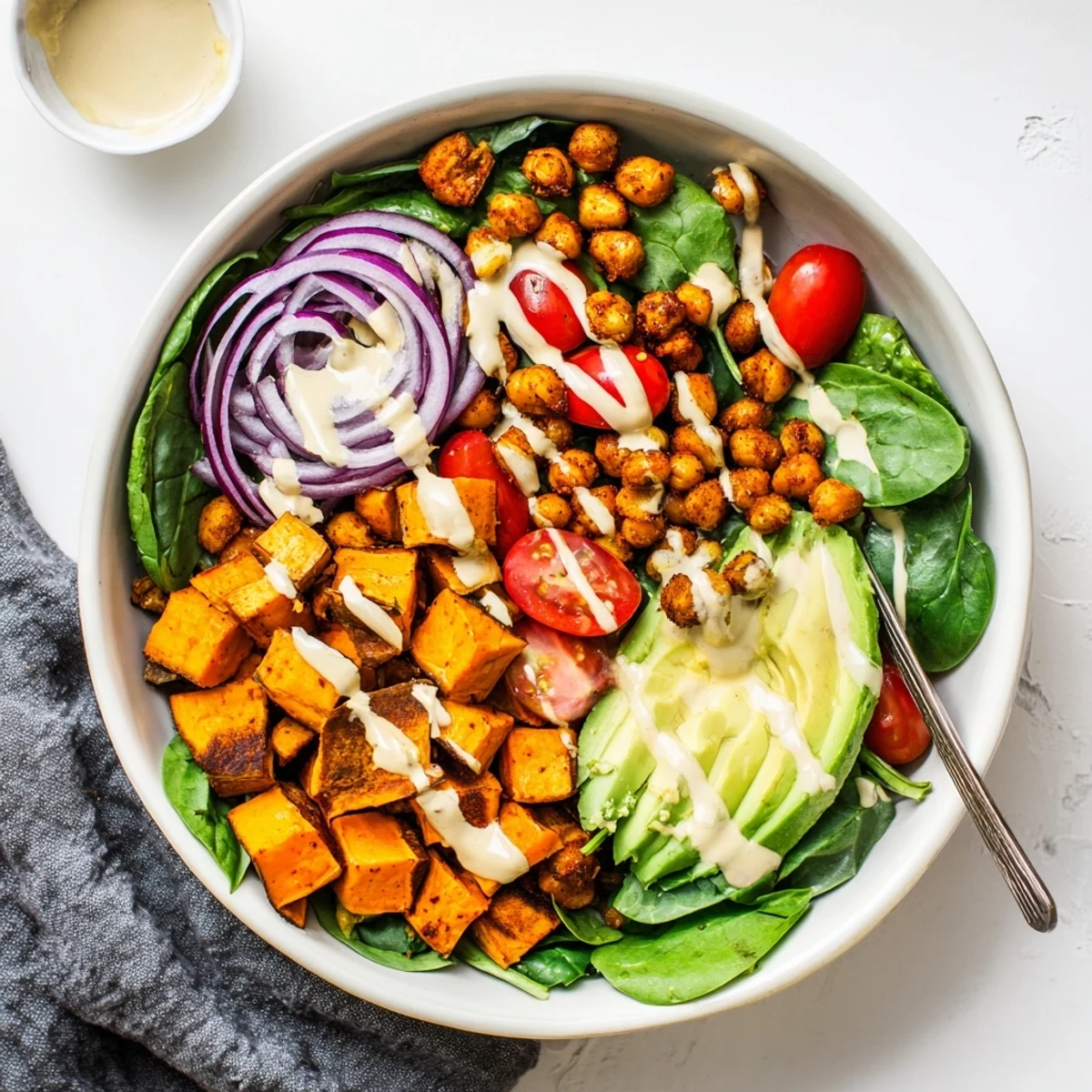 Colorful hearty sweet potato bowl with roasted chickpeas and creamy tahini dressing drizzled over fresh vegetables
