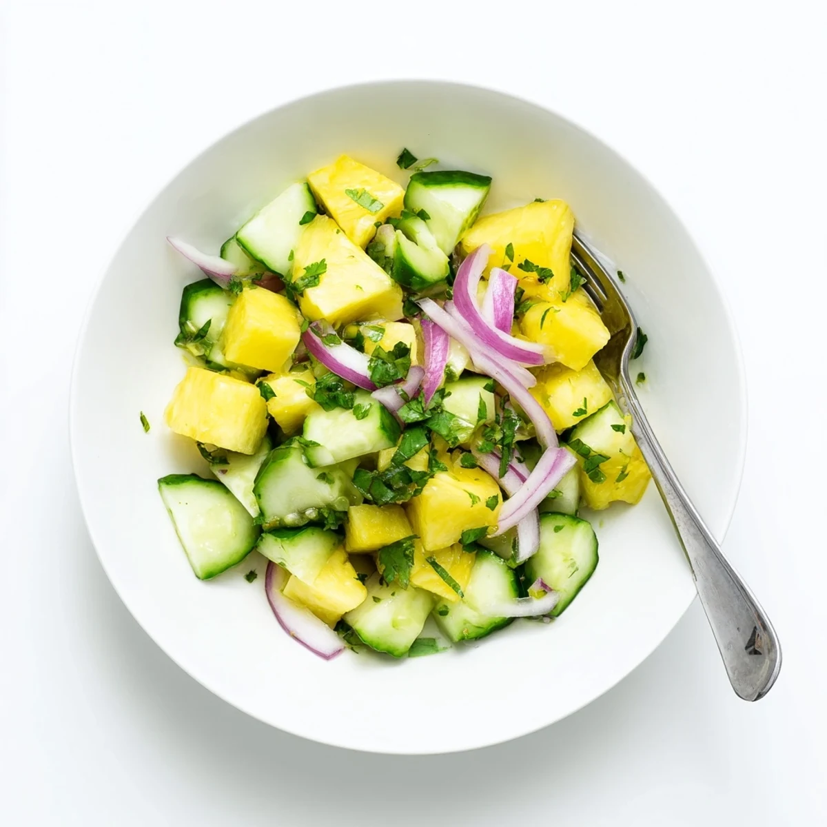Colorful pineapple cucumber salad in white serving dish featuring red onion and fresh herbs