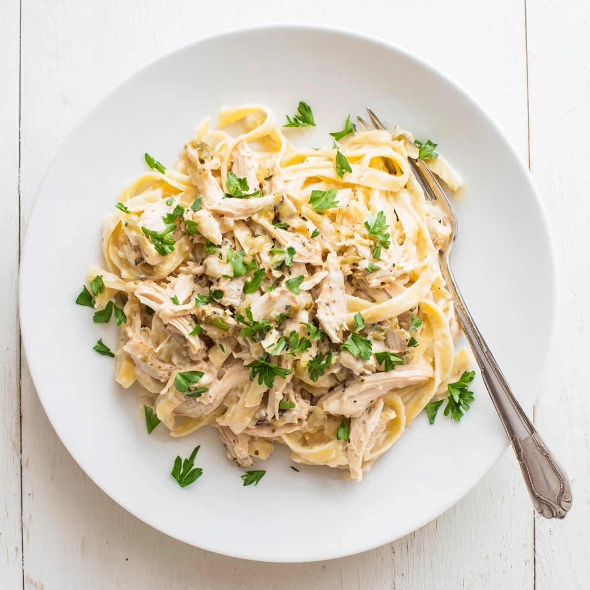 Slow cooker Chicken Alfredo pasta dish garnished with fresh parsley and served in a white bowl