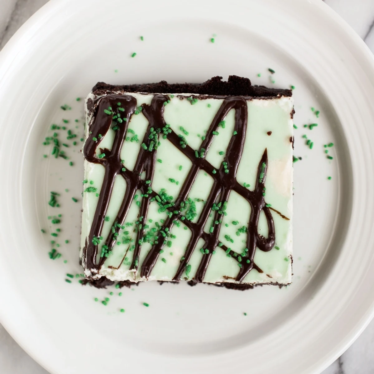 Decadent green St. Patricks Irish Mint Cheesecake Fudge Squares with dark chocolate drizzle on chocolate cookie crust