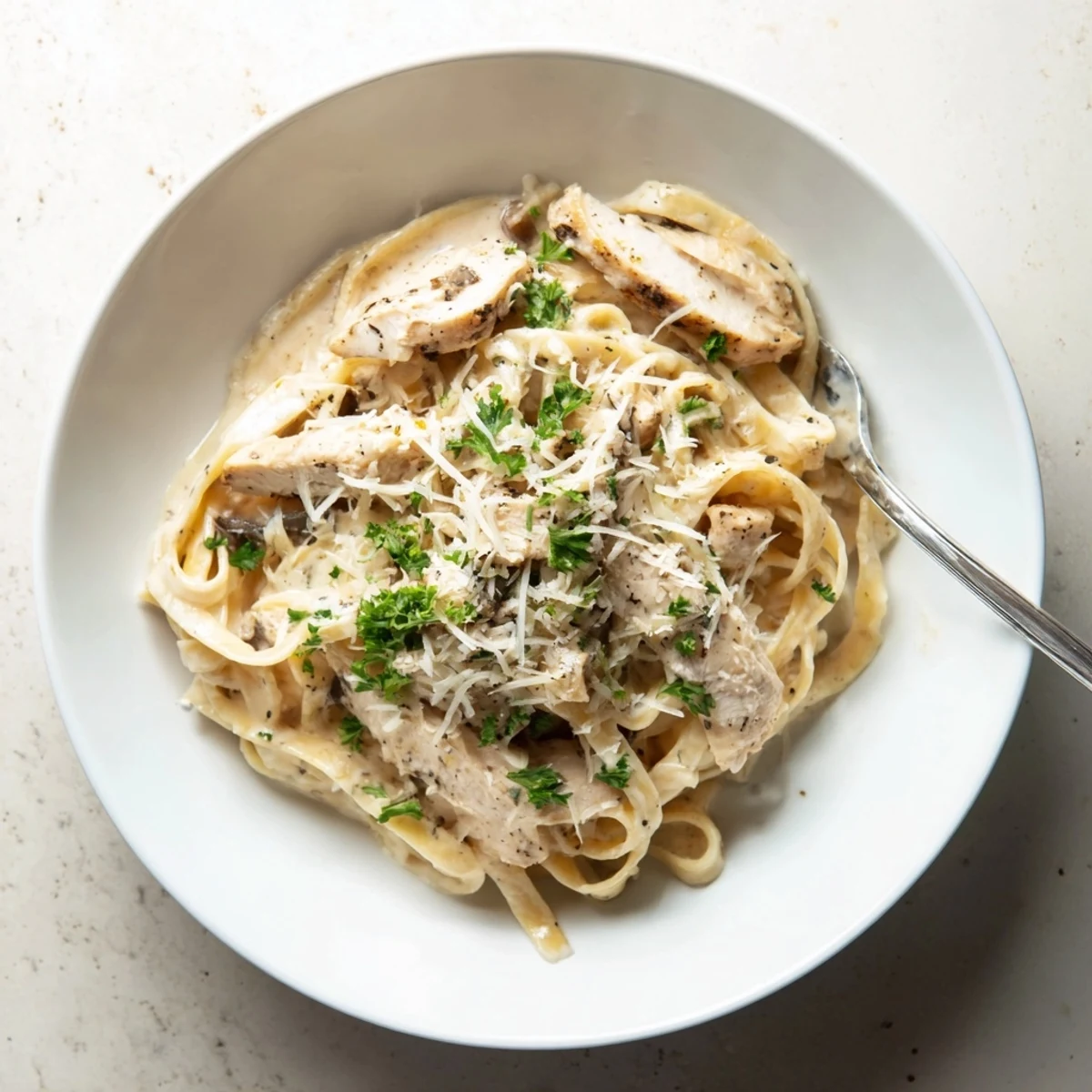 Heaping bowl of garlic parmesan chicken pasta topped with tender chicken pieces and fresh parsley garnish