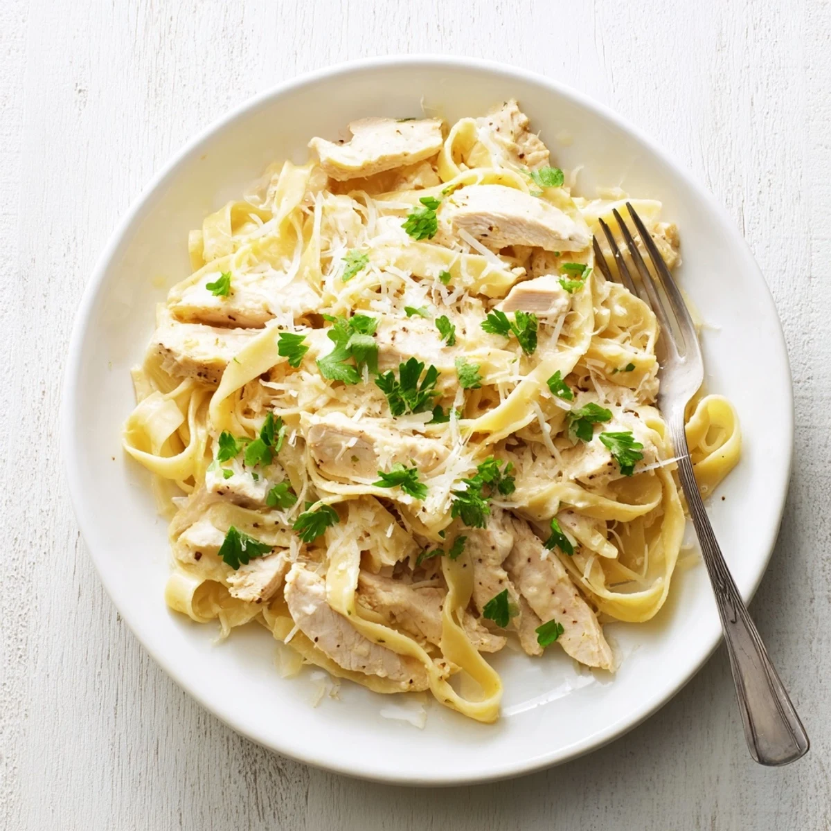 Golden strands of garlic parmesan chicken pasta coated in creamy white sauce with sliced chicken breast