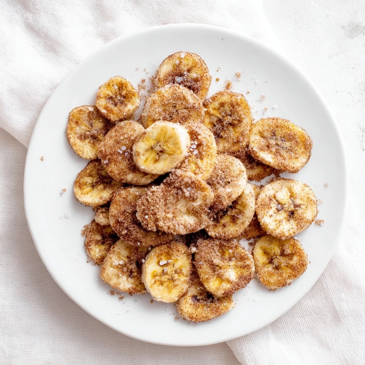 Golden brown cinnamon sugar air fryer banana chips arranged on a white serving plate