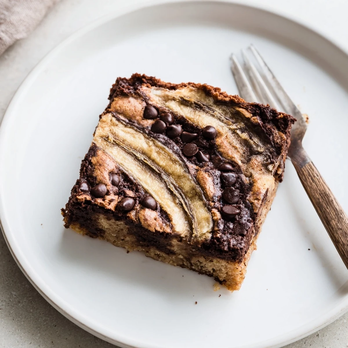 Decadent chocolate brownie batter swirled with sweet banana bread batter, sliced into squares with a fork nearby