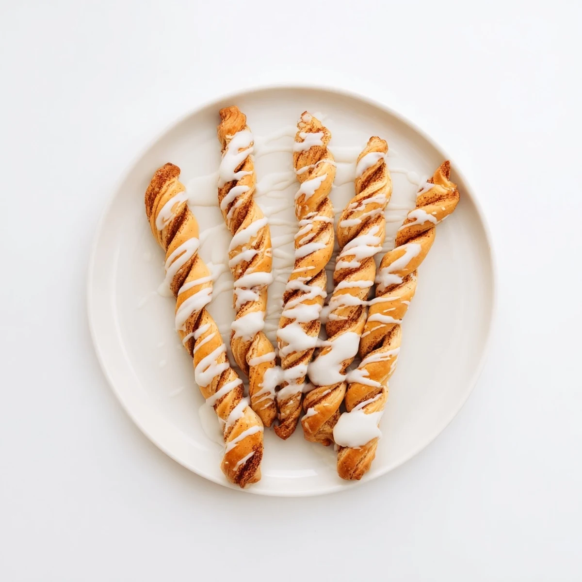 Golden sweet cinnamon twists drizzled with vanilla glaze on a white serving plate