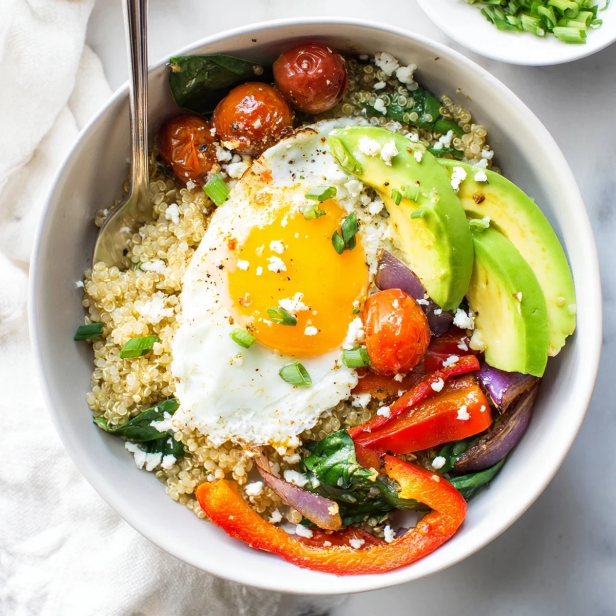 Golden fried egg atop fluffy quinoa breakfast bowl with colorful sautéed vegetables and fresh herbs