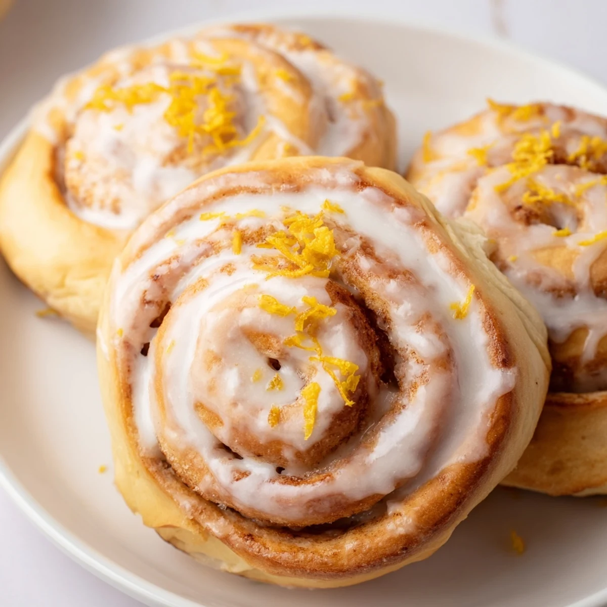 Golden homemade lemon rolls drizzled with tangy glaze on a rustic baking dish
