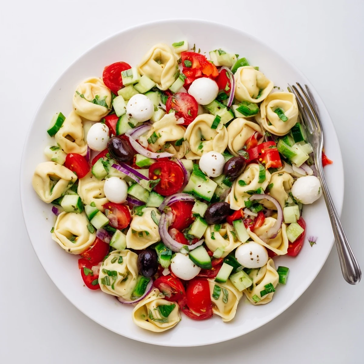 Colorful tortellini pasta salad in a serving bowl with cherry tomatoes, cucumber, and fresh basil