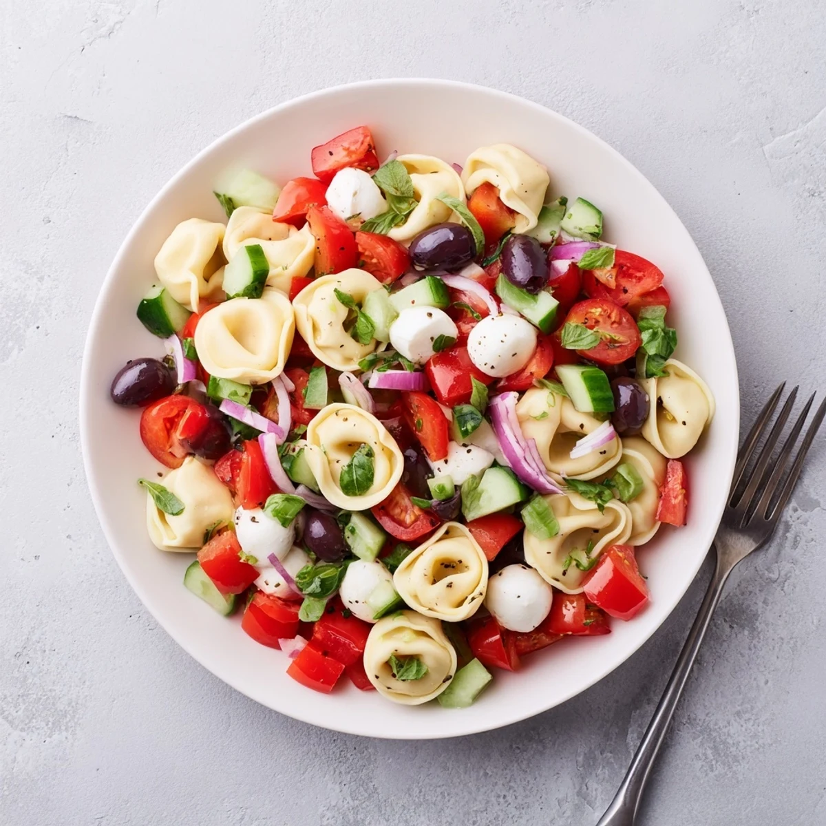 Cheese tortellini pasta salad tossed with crisp vegetables and zesty Italian dressing glistening