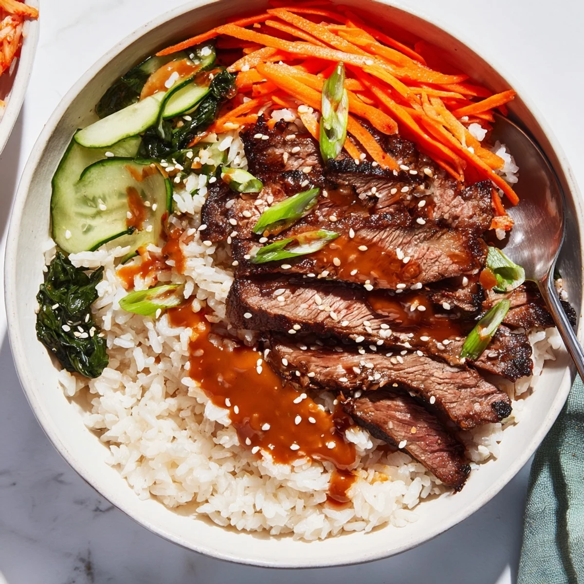 A hearty Korean BBQ steak rice bowl topped with sesame seeds, fresh greens, and a creamy spicy drizzle