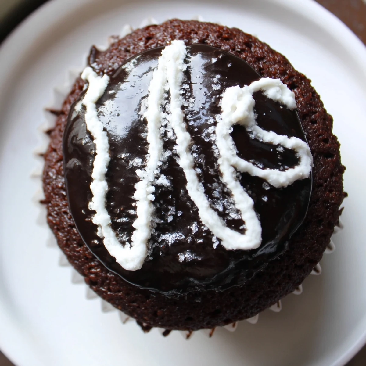 A Homemade Hostess Cupcake topped with shiny glaze and a classic white icing swirl