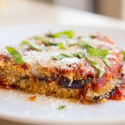 Fresh basil garnish tops this homemade baked eggplant parmesan, served with crusty bread and salad.
