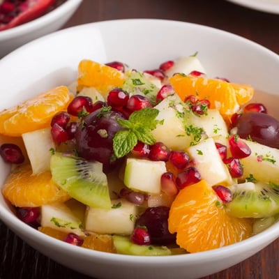 Bright overhead view of Winter Fruit Salad with Fresh Mint and Lime, featuring glossy red grapes, crisp pear chunks, and a sparkling lime zest garnish on a rustic wooden table.