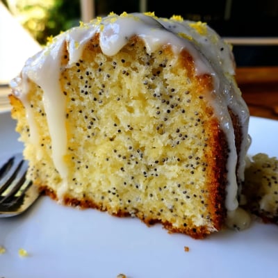 A slice of moist Lemon Poppy Seed Cake reveals a tender crumb flecked with poppy seeds.