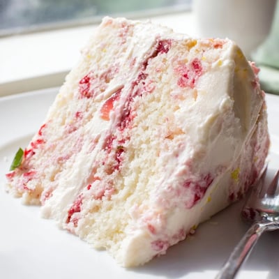 Freshly frosted Strawberry Lemonade Cake With Creamy Lemon Buttercream with vibrant pink layers and tangy buttercream on a sunny patio table.