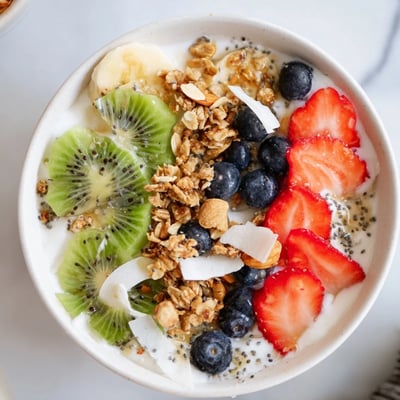 Healthy Breakfast Bowl with Greek yogurt, chia seeds, mixed fruits, almonds, and toasted granola beside a glass of green tea at breakfast.