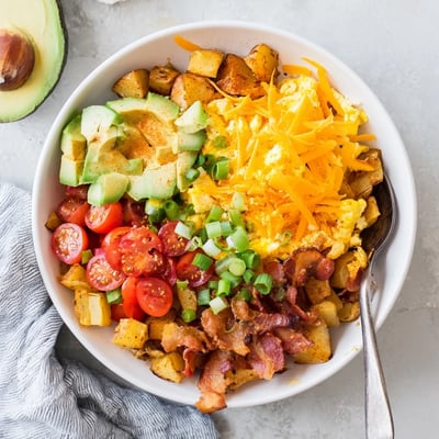 A colorful Loaded Breakfast Bowl topped with diced avocado, bacon, and fresh green onions for serving.
